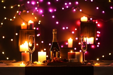 Photo of Romantic dinner table setting with burning candles and festive lights