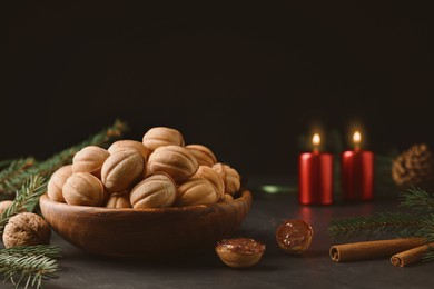 Photo of Homemade walnut shaped cookies with boiled condensed milk, cinnamon sticks, candles and fir branches on black table, space for text