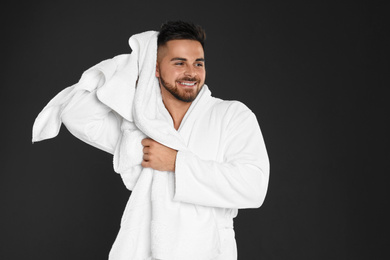 Photo of Young man in bathrobe drying hair with towel on black background