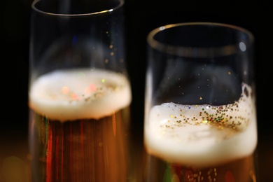 Glasses of champagne with golden glitter on dark background, closeup