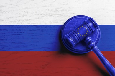 Image of Judge's gavel on wooden background in colors of Europenean Union and Russian flags, top view. Concept of sanctions against Russia