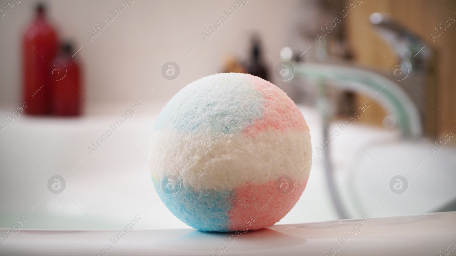 Photo of Colorful bath bomb on tub indoors. Spa product