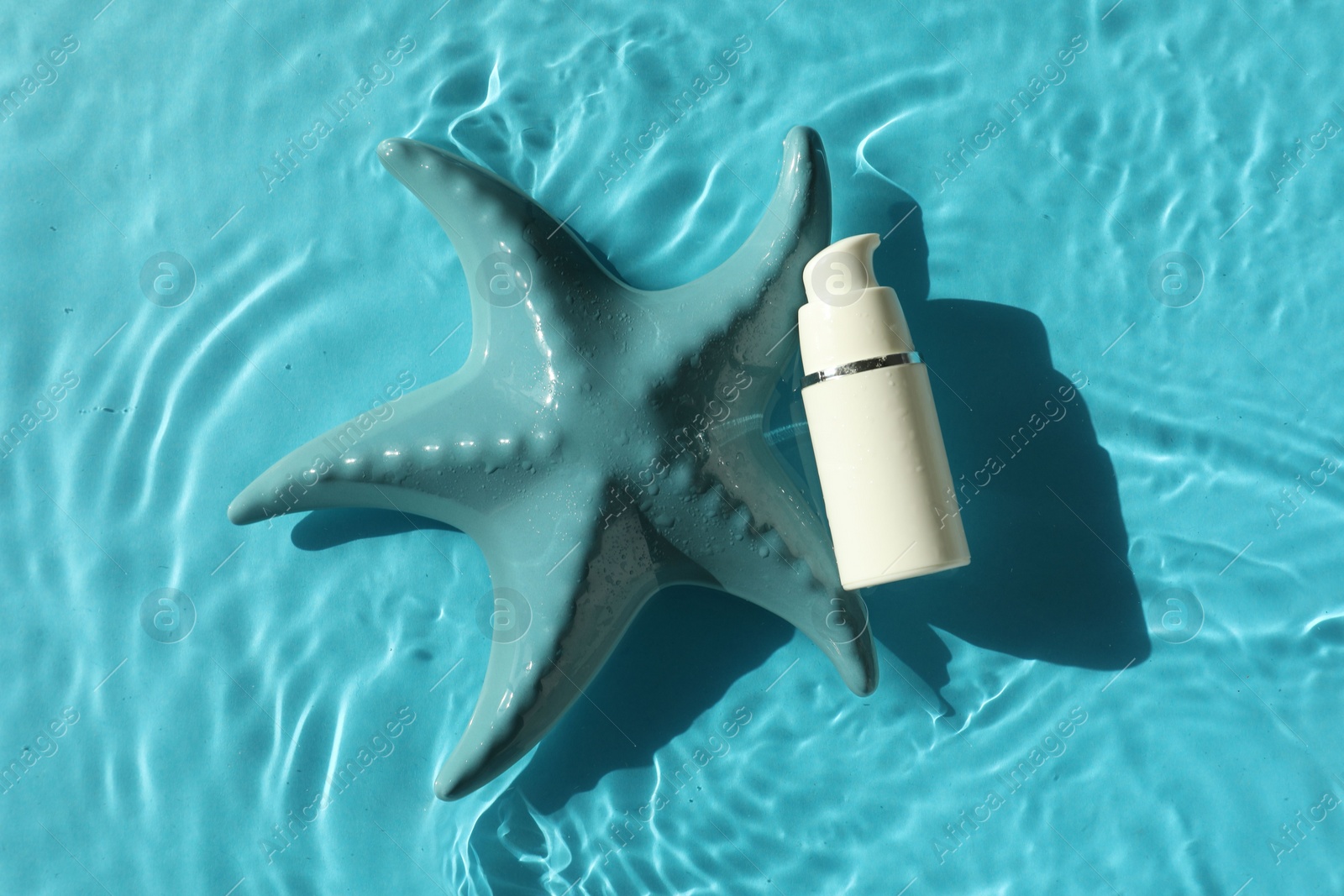 Photo of Moisturizing cream and sea star in water on light blue background, top view
