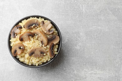 Photo of Delicious bulgur with mushrooms in bowl on gray table, top view. Space for text