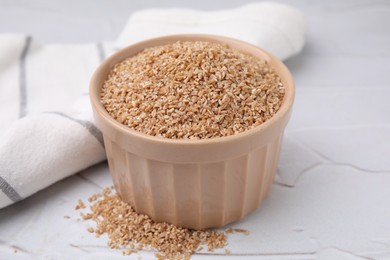 Dry wheat groats in bowl on white textured table, closeup