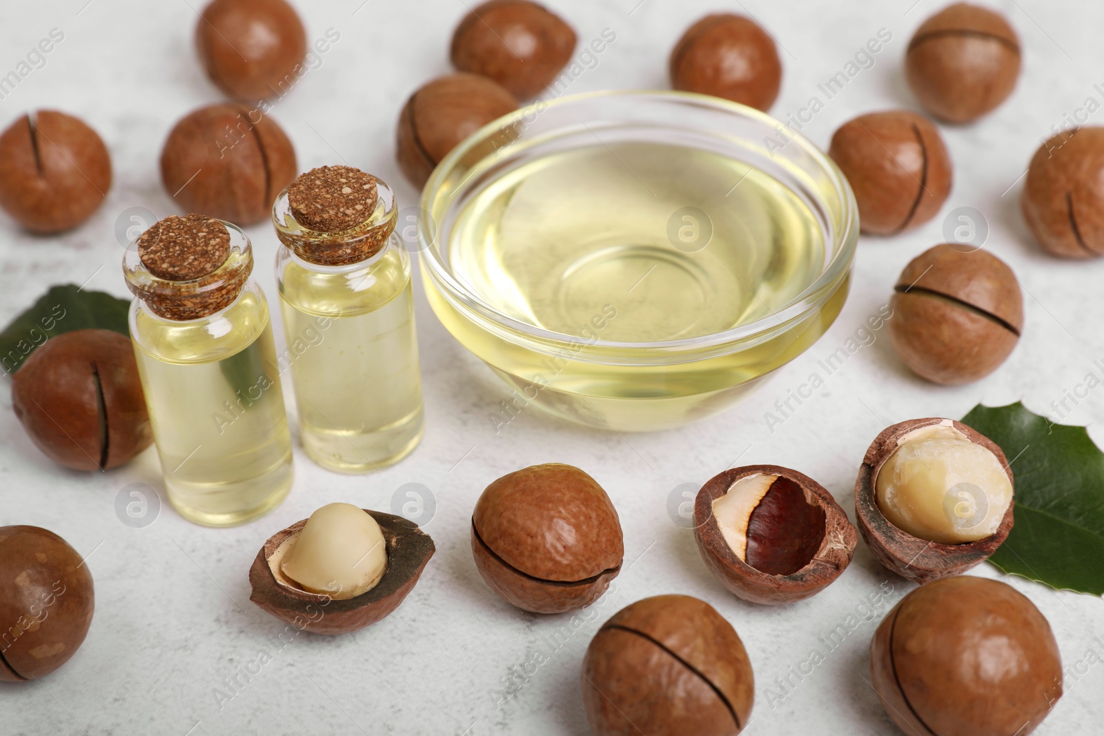 Photo of Delicious organic Macadamia nuts and natural oil on white textured table, closeup