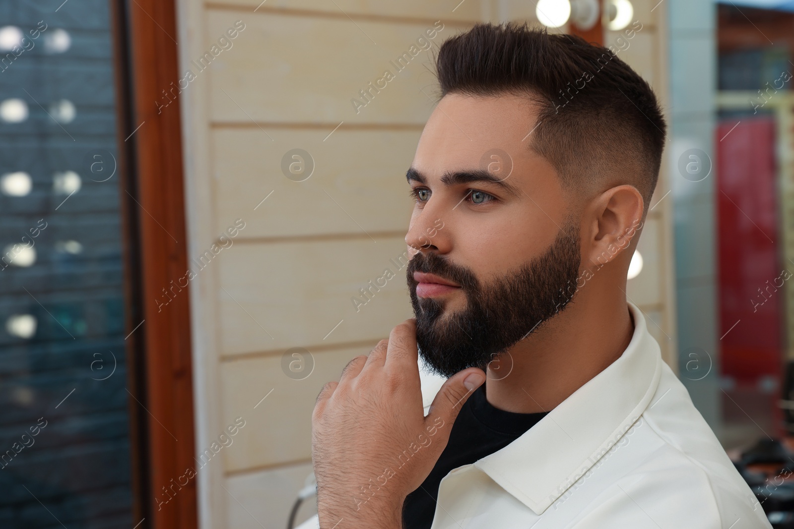 Photo of Young man with fresh haircut and groomed beard in barbershop
