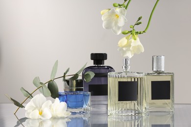 Luxury perfumes and floral decor on mirror surface against light grey background