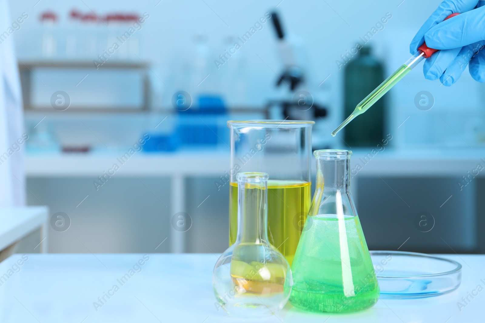 Photo of Laboratory analysis. Woman dripping liquid into flask at white table indoors, closeup