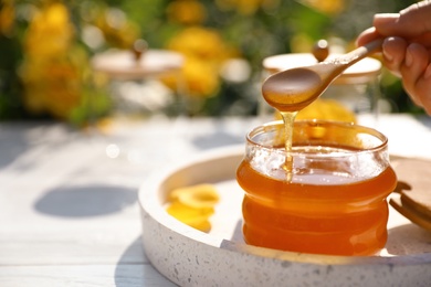 Photo of Woman pouring honey into glass jar at white wooden table, closeup. Space for text