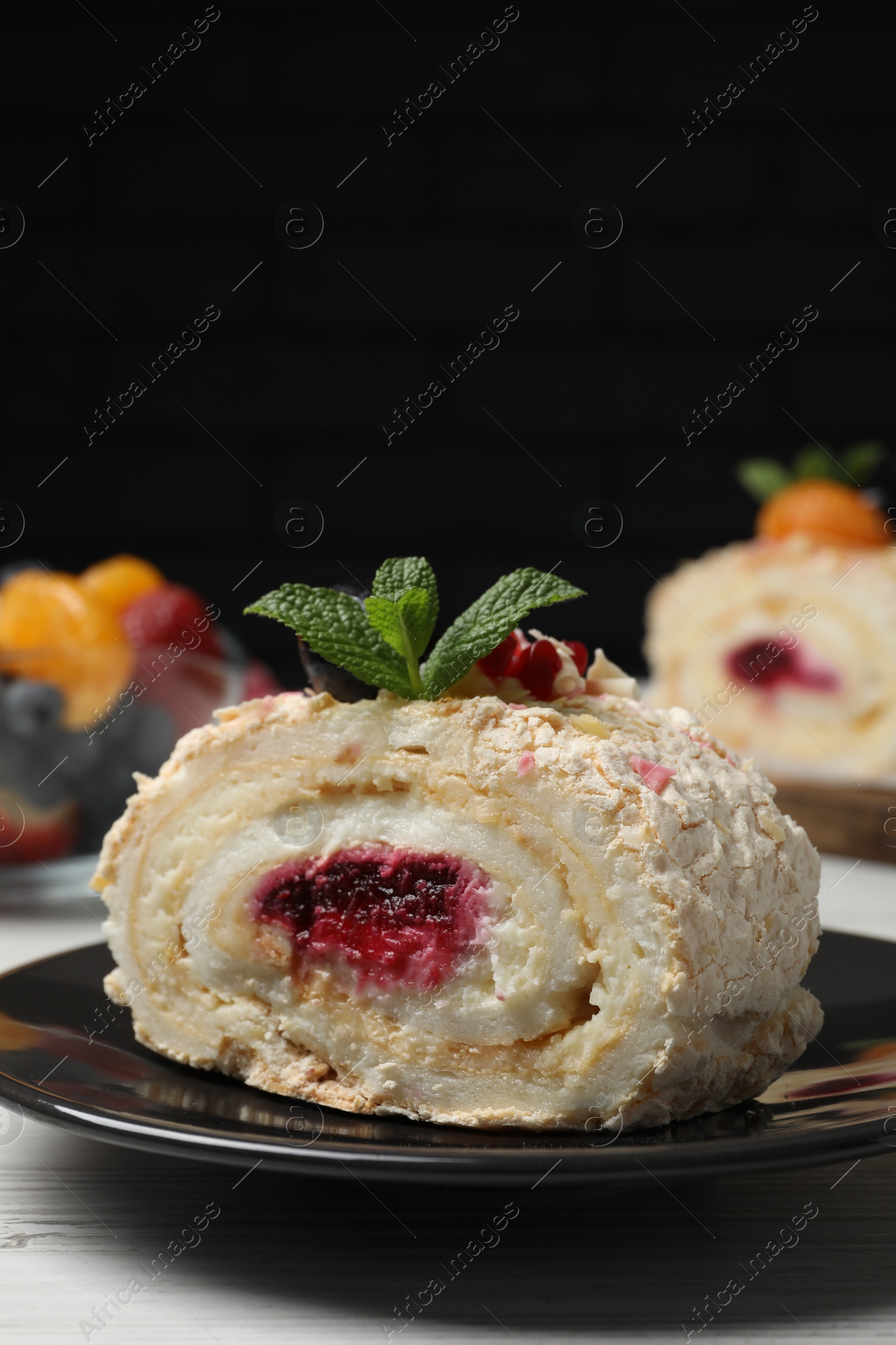 Photo of Slice of tasty meringue roll with jam and mint leaves on white wooden table, closeup