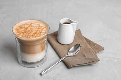 Glass of caramel macchiato and gravy jug with sauce on table