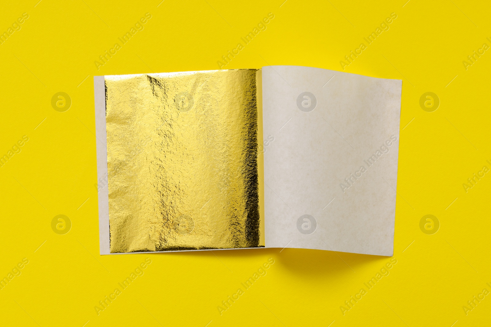 Photo of Edible gold leaf sheet on yellow background, top view