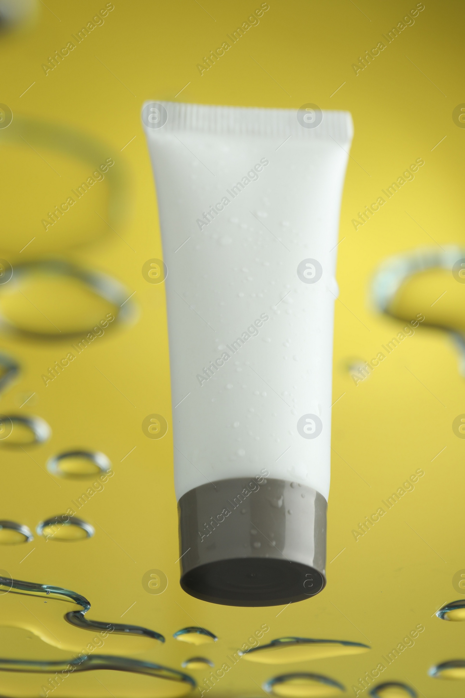 Photo of Moisturizing cream in tube on glass with water drops against yellow background, low angle view