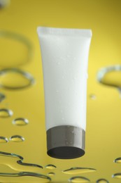 Moisturizing cream in tube on glass with water drops against yellow background, low angle view