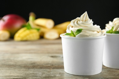 Cups with tasty frozen yogurt on wooden table. Space for text