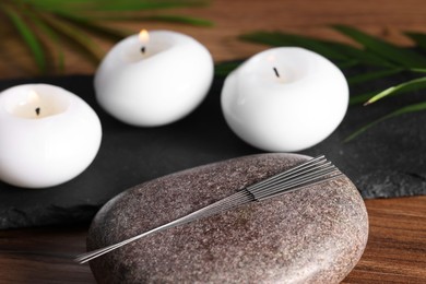 Photo of Stone with acupuncture needles and burning candles on wooden table