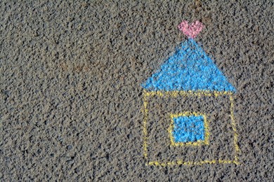 Photo of House with heart drawn by blue and yellow chalk on asphalt, top view. Space for text