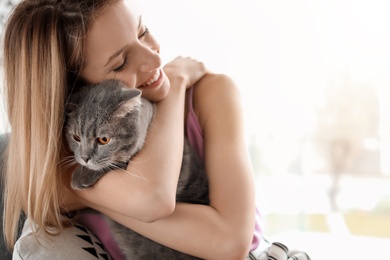 Photo of Young woman with her cute pet cat in armchair at home