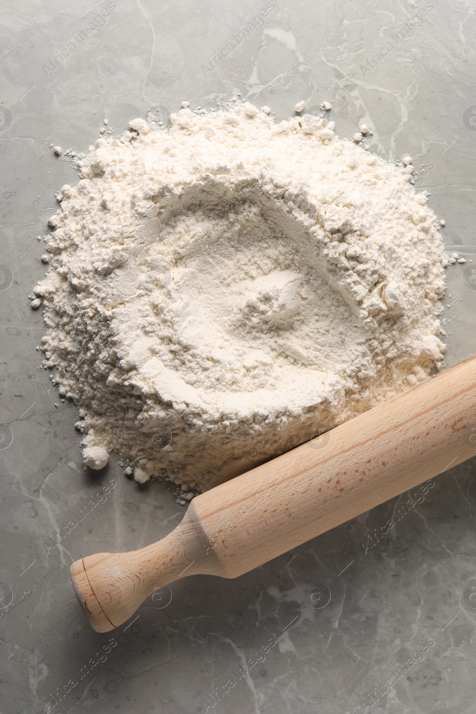 Photo of Pile of flour and rolling pin on grey marble table, top view