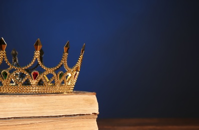Photo of Beautiful golden crown on old books against dark blue background, space for text. Fantasy item