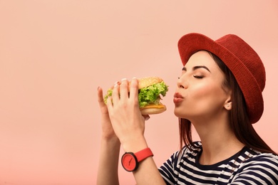 Young woman eating tasty burger on color background. Space for text