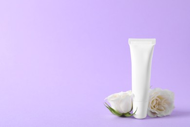 Photo of Lip balm and white rose flowers on lilac background, space for text