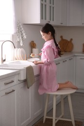Little girl washing dishes in kitchen at home
