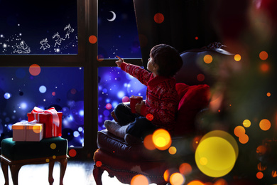 Cute little boy waiting for Santa Claus near window at home. Christmas holiday