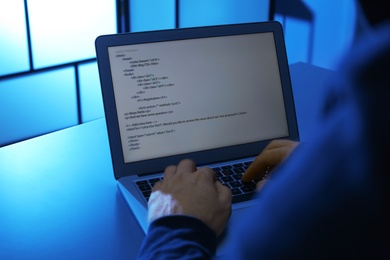 Photo of Man using laptop at table in dark room, closeup. Criminal offence