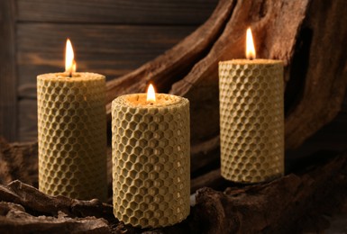 Photo of Beautiful burning beeswax candles on snag near wooden wall