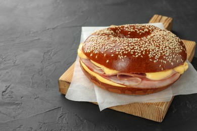 Photo of Delicious bagel with ham and cheese on grey textured table, space for text