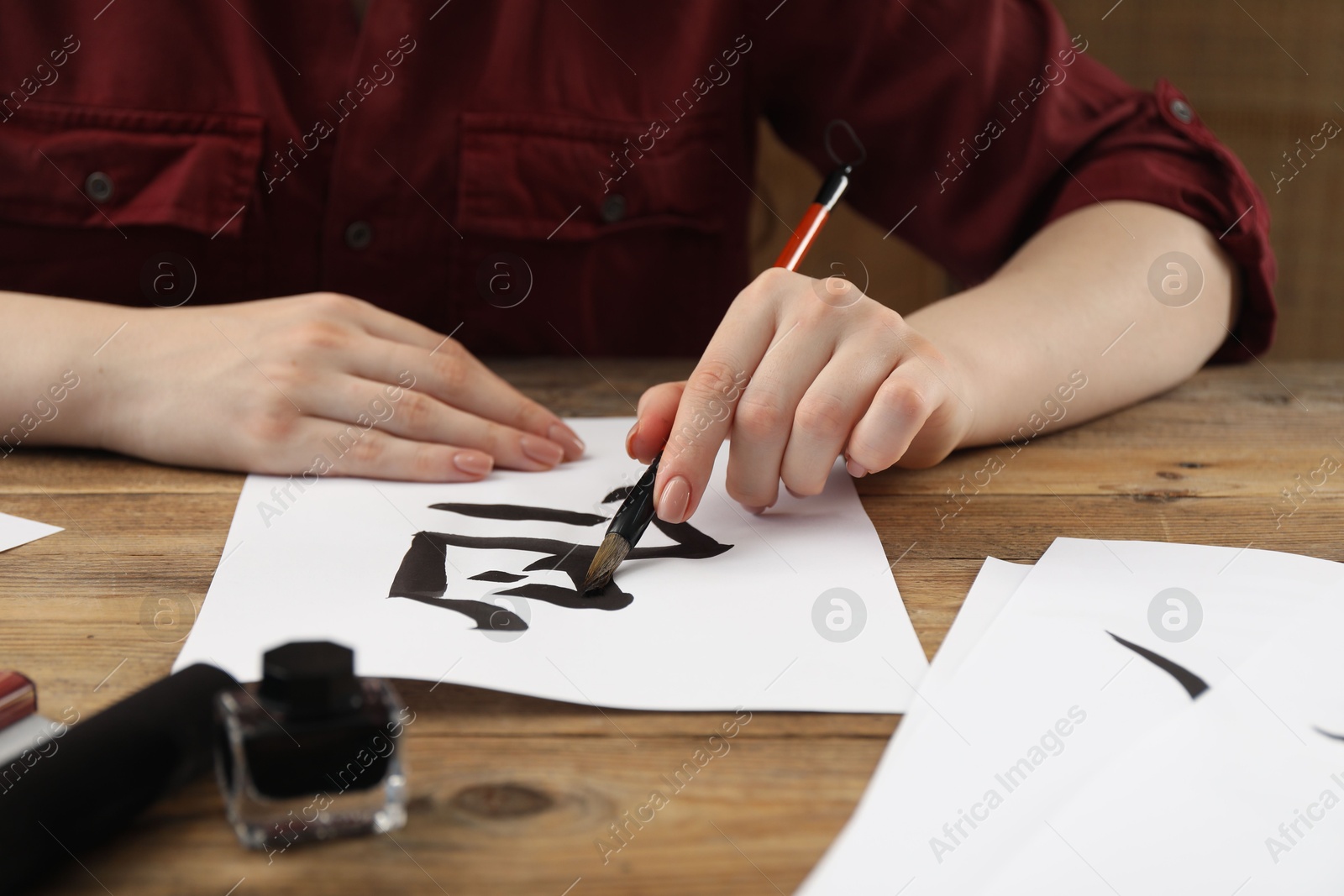 Photo of Calligraphy. Woman with brush and inkwell writing hieroglyphs on paper at wooden table, closeup