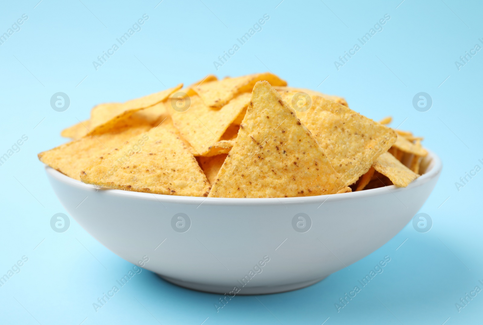 Photo of Bowl of tasty Mexican nachos chips on light blue background