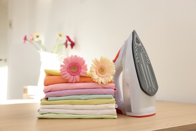 Photo of Stack of clean clothes, modern iron and flowers on wooden table