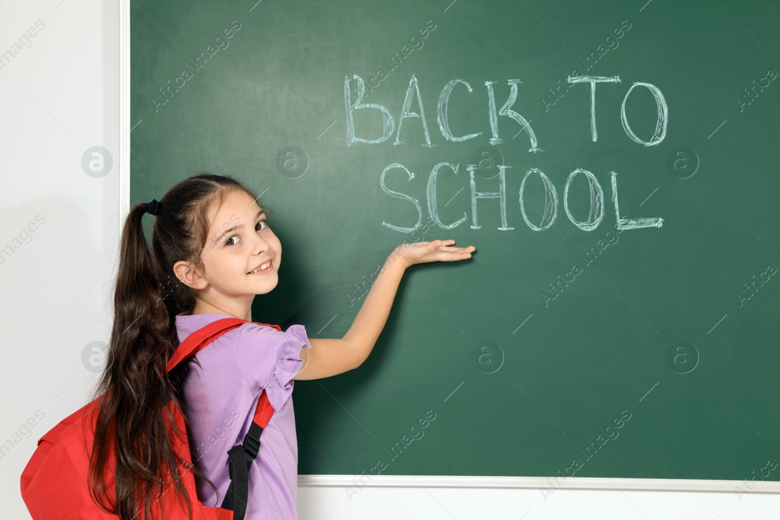 Photo of Little child near chalkboard with text BACK TO SCHOOL