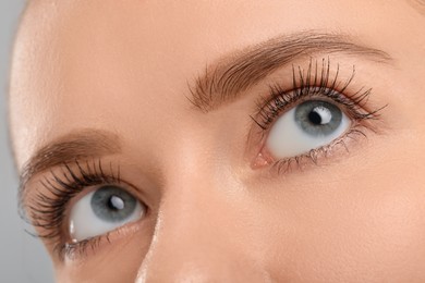 Photo of Woman with long eyelashes after mascara applying against grey background, closeup