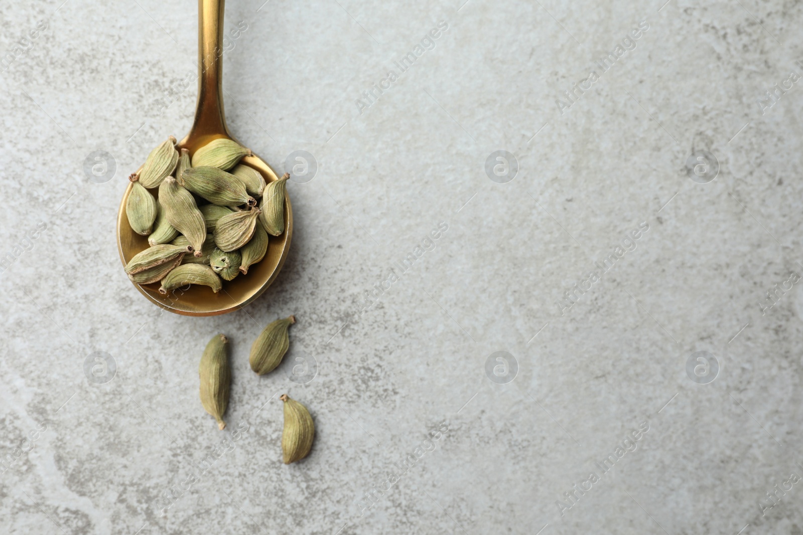 Photo of Spoon with dry cardamom pods on light table. Space for text