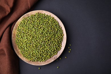 Photo of Wooden bowl with green mung beans and napkin on black background, flat lay. Space for text