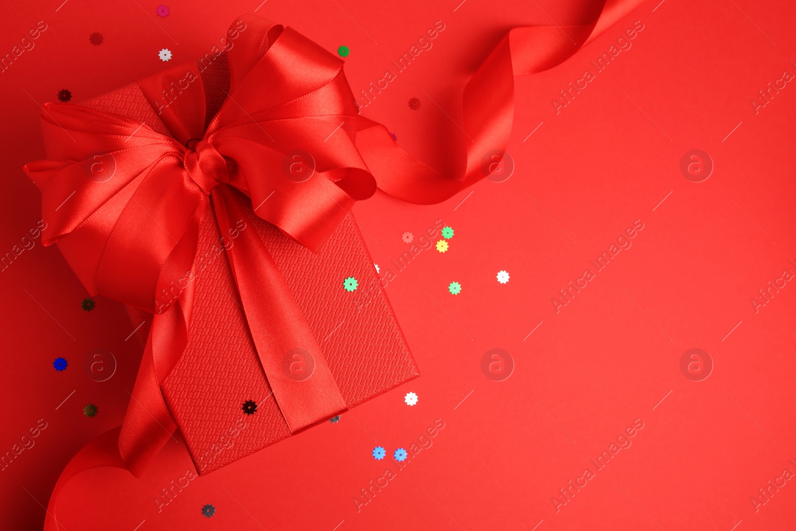 Photo of Beautiful gift box with bow and confetti on red background, top view. Space for text