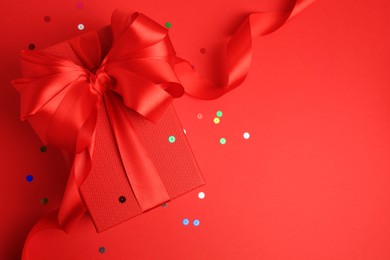 Photo of Beautiful gift box with bow and confetti on red background, top view. Space for text