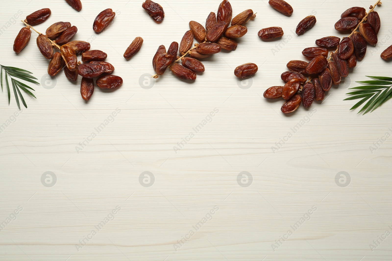 Photo of Tasty sweet dried dates with green leaves on white wooden table, flat lay. Space for text