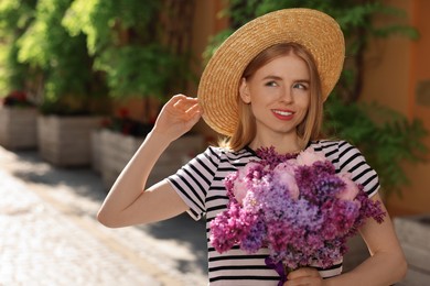 Beautiful woman with bouquet of spring flowers on city street, space for text