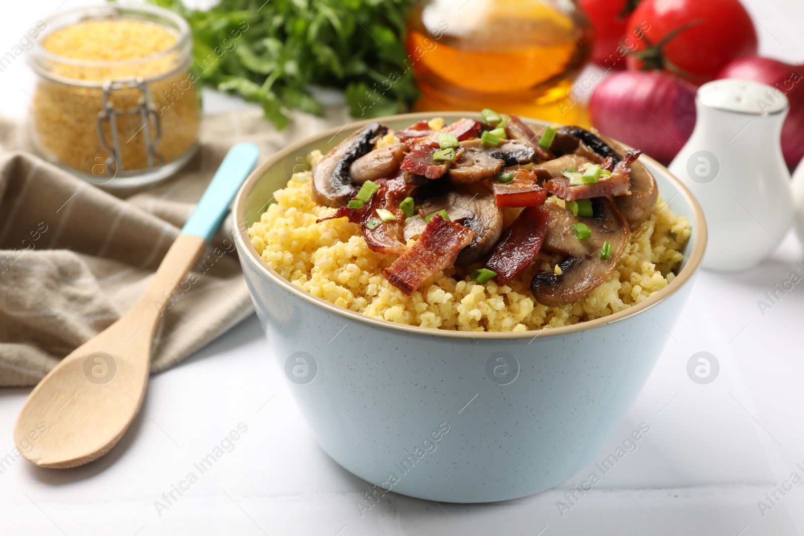 Photo of Tasty millet porridge with mushrooms, bacon and green onion in bowl on white table, closeup