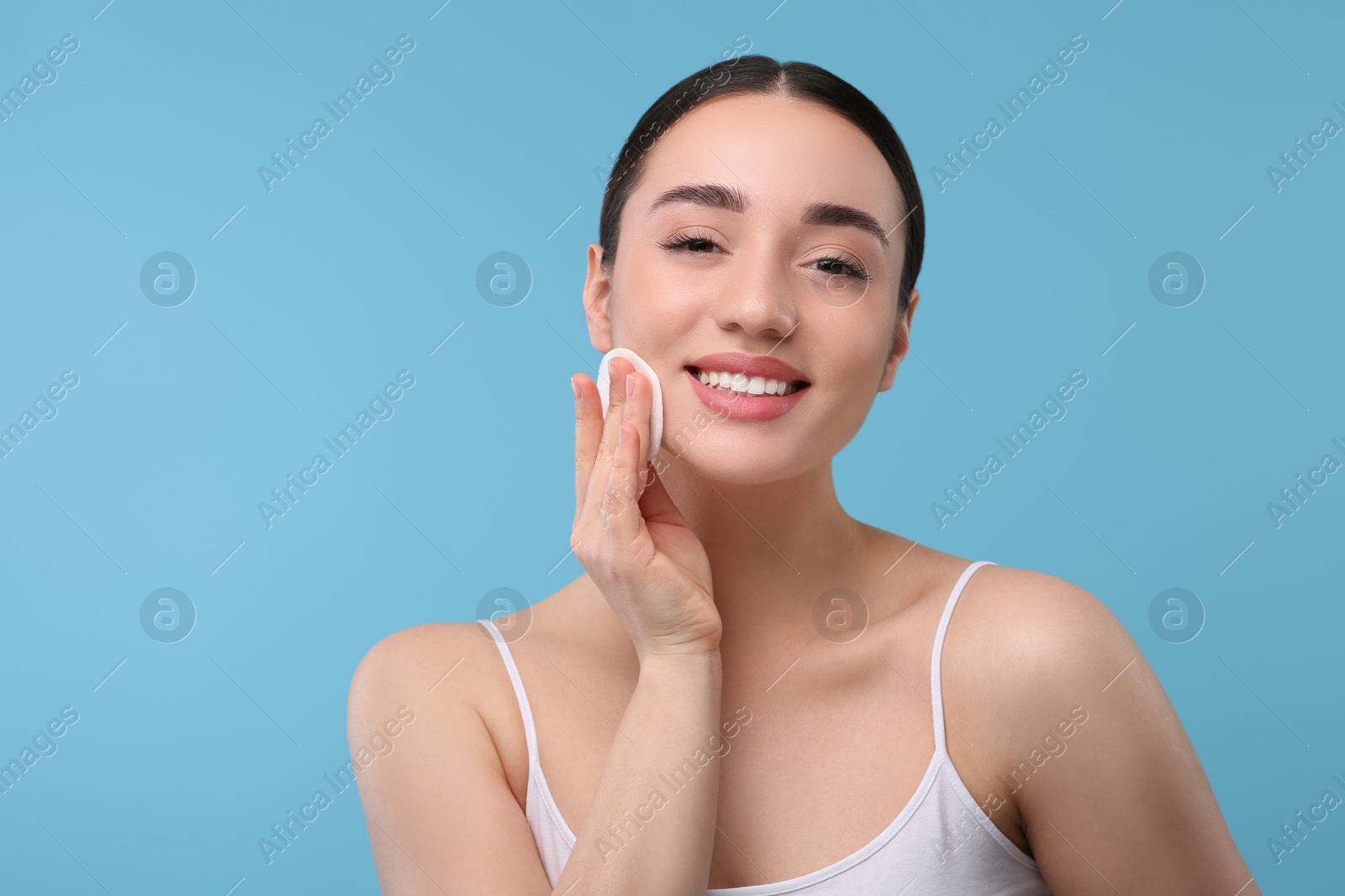 Photo of Beautiful woman removing makeup with cotton pad on light blue background