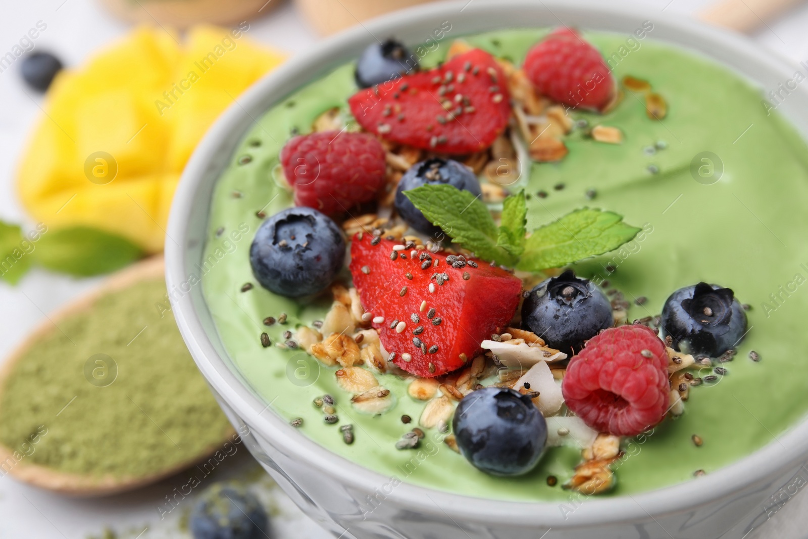 Photo of Tasty matcha smoothie bowl served with berries and oatmeal on white table, closeup. Healthy breakfast