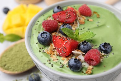 Tasty matcha smoothie bowl served with berries and oatmeal on white table, closeup. Healthy breakfast