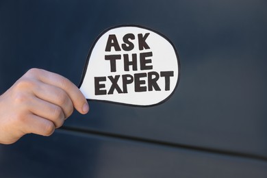 Photo of Man holding card with phrase Ask The Expert near black wall, closeup