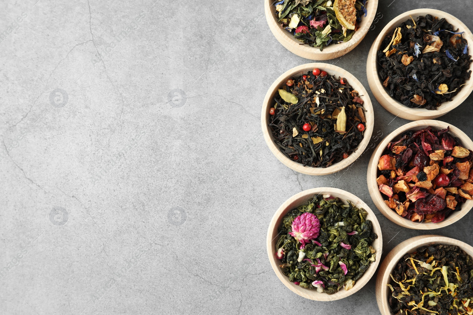 Photo of Different kinds of dry herbal tea in wooden bowls on light grey table, flat lay. Space for text