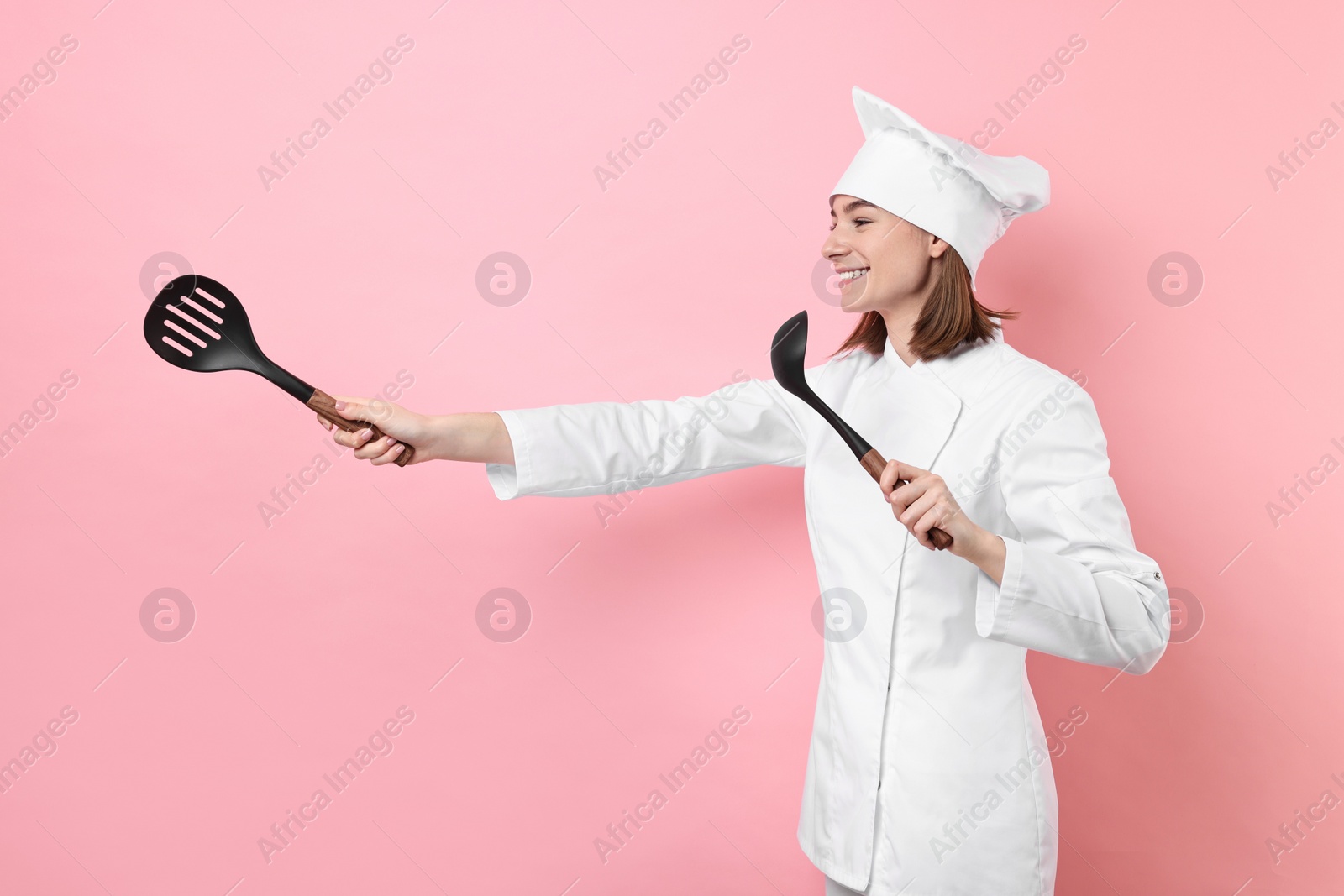 Photo of Professional chef with skimmer and ladle having fun on pink background